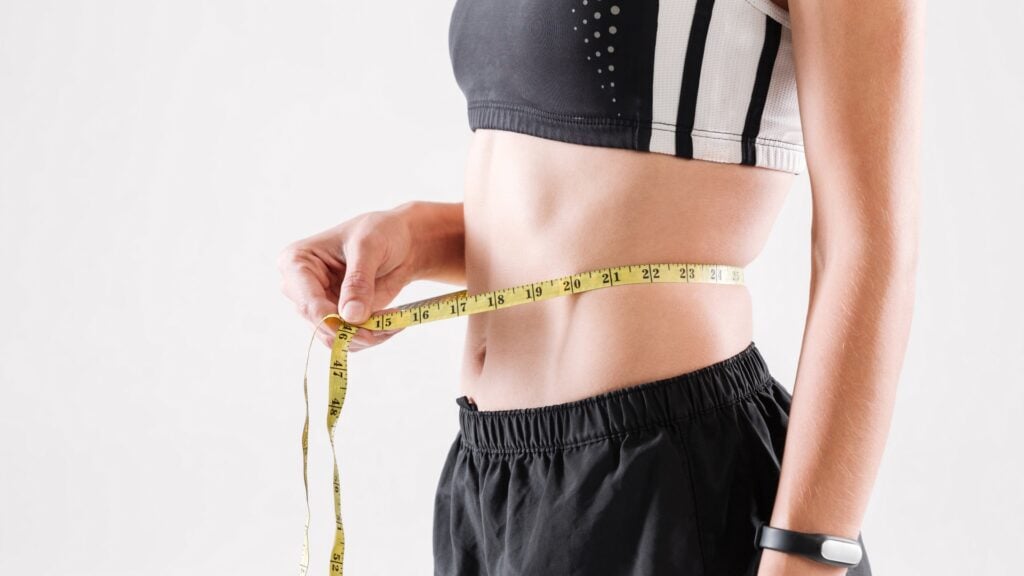 Person measuring waist with yellow tape measure.