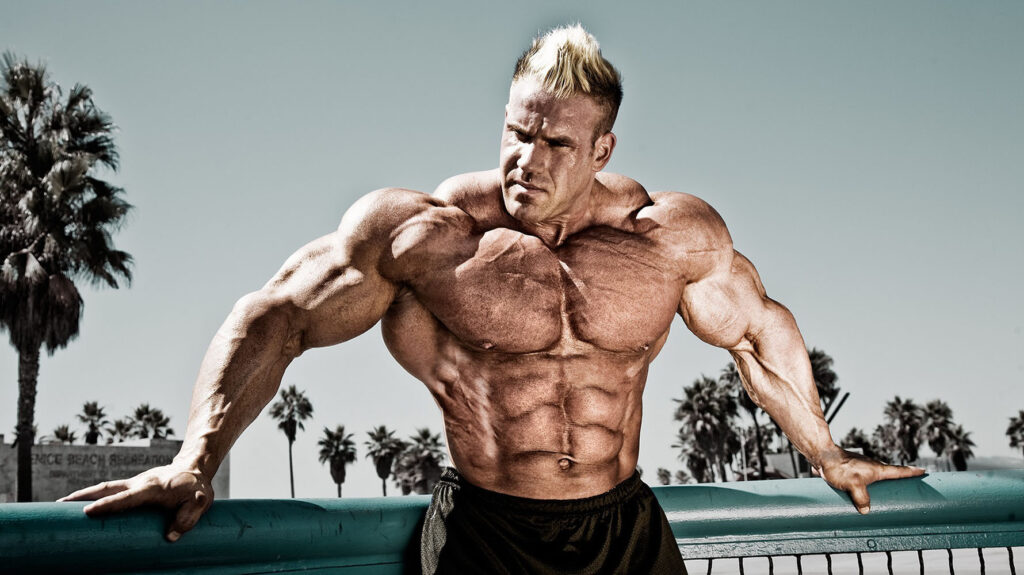 Bodybuilder posing outdoors with palm trees.