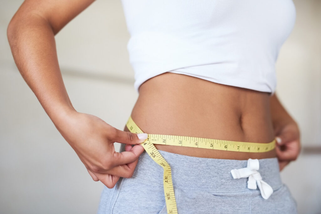 Person measuring waist with yellow tape measure.
