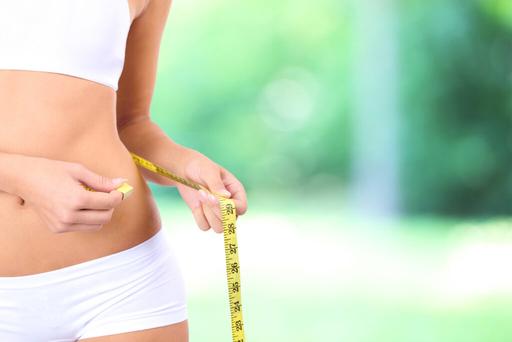 Person measuring waist with tape measure.