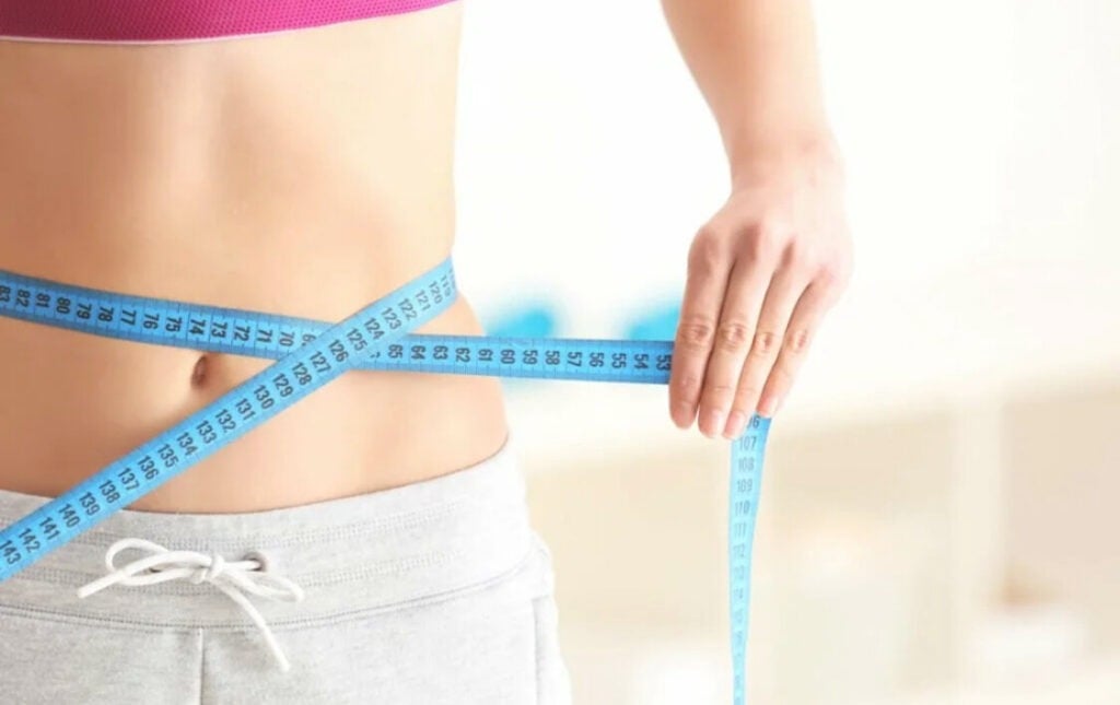 Person measuring waist with blue tape measure.