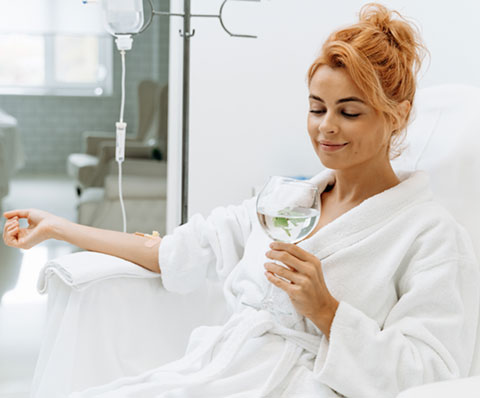 Woman relaxing with IV therapy and drink.